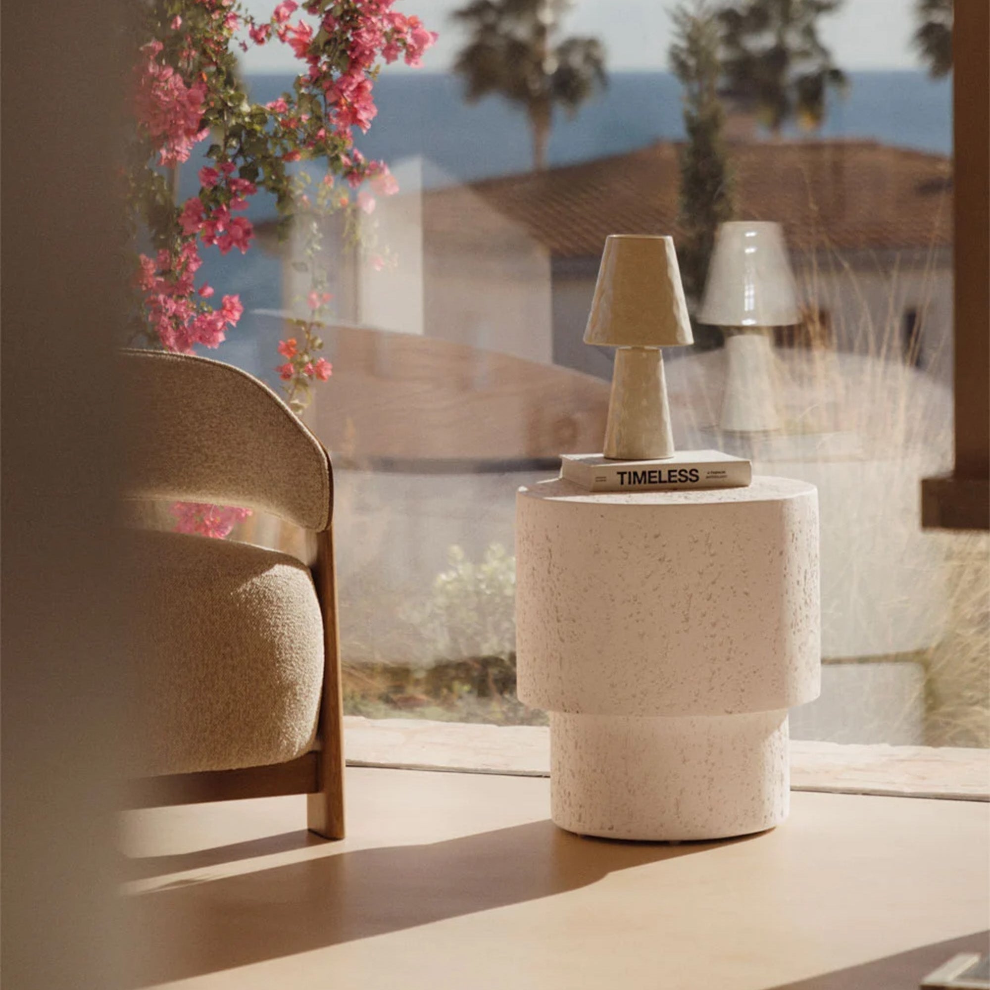 Apvalus šoninis staliukas, kurio pagrindas siauresnis nei korpusas, pagamintas iš cemento, o jo spalva yra balta. 